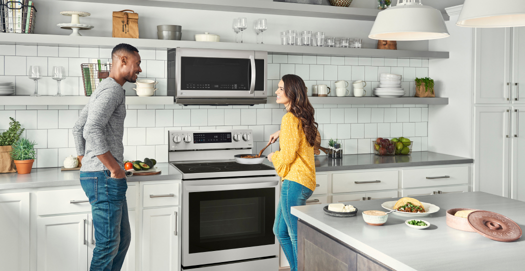 a man and a woman cooking in a kitchen with white tiles and white cabinets and stainless steel appliances